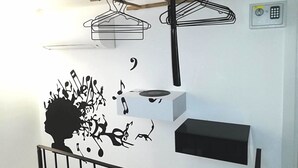 Ein Zimmer mit weißer Wand, einer schwarzen Silhouette eines Baumes mit Noten, einem hängenden Kleiderständer und einer kleinen schwarzen Schachtel.
