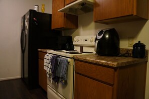 Kitchen area with a stove, coffee maker, and refrigerator, complete with cabinets and a countertop.