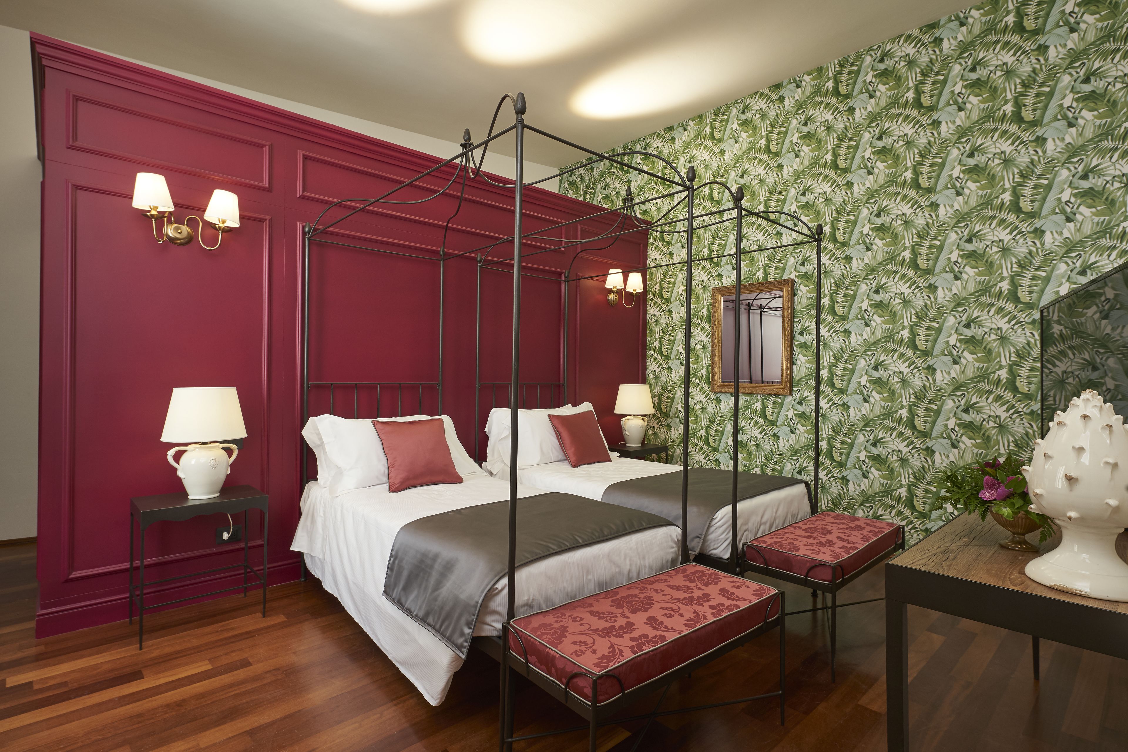 A four-poster bed with a canopy, two bedside tables with lamps, a wooden bench, and a patterned wallpaper.