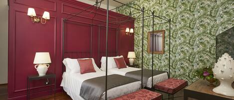 A four-poster bed with a canopy, two bedside tables with lamps, a wooden bench, and a patterned wallpaper.
