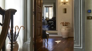 En hall som leder till en matplats med en dörr av trä, en dörrmatta med texten ”PERUZZI URBAN RESIDENCES” och en krukväxt.