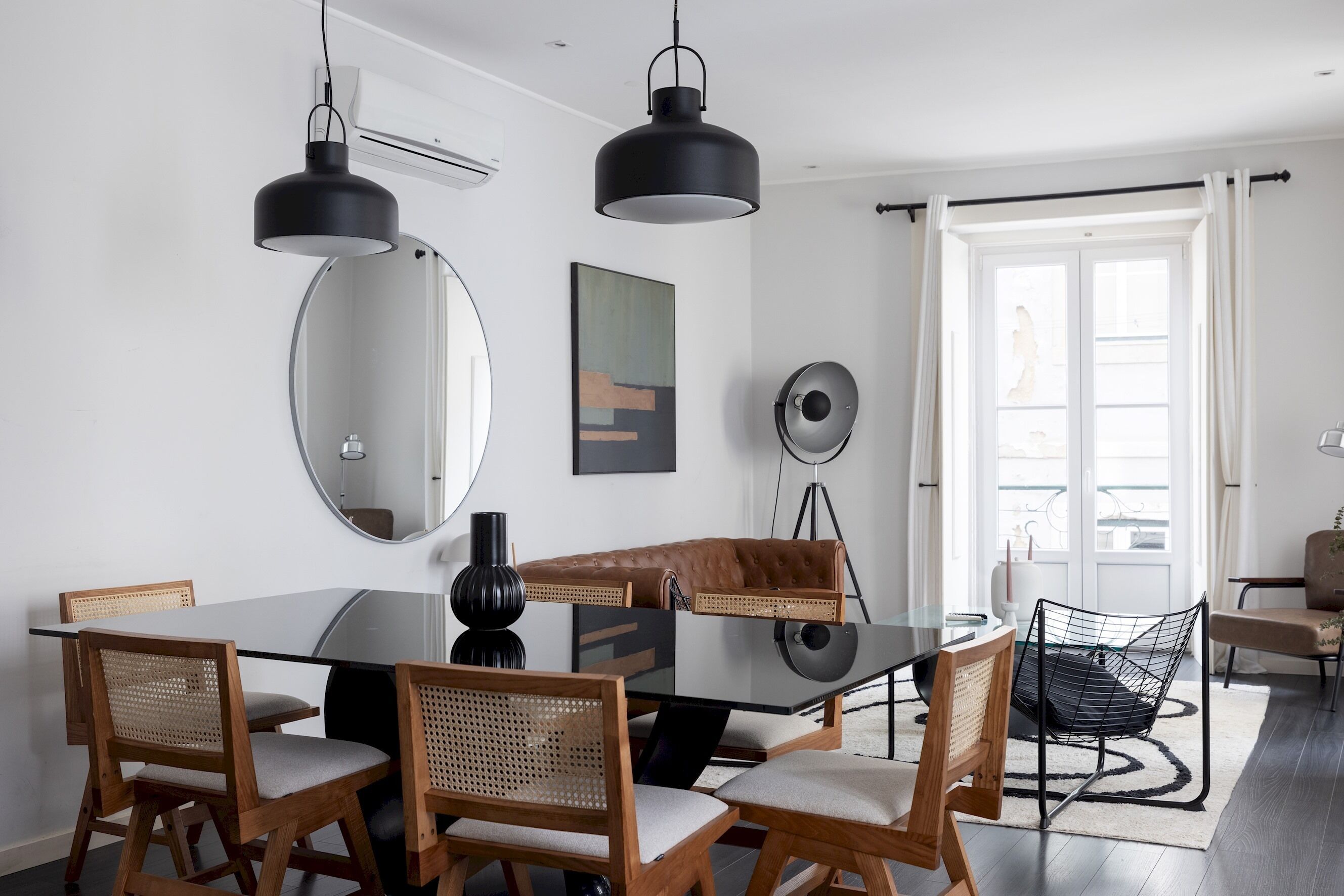 Un espace de salle à manger moderne avec une table en verre, des chaises en bois et des suspensions noires.