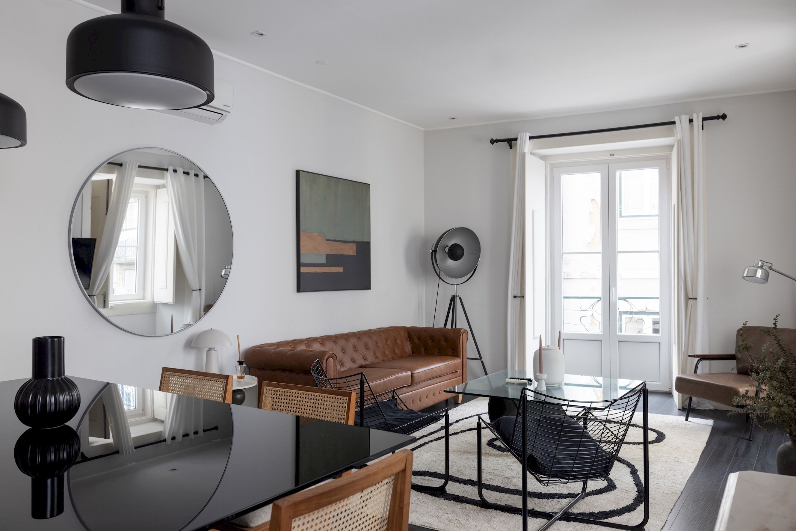A modern living room with a brown leather sofa, a glass coffee table, and a round mirror on the wall.