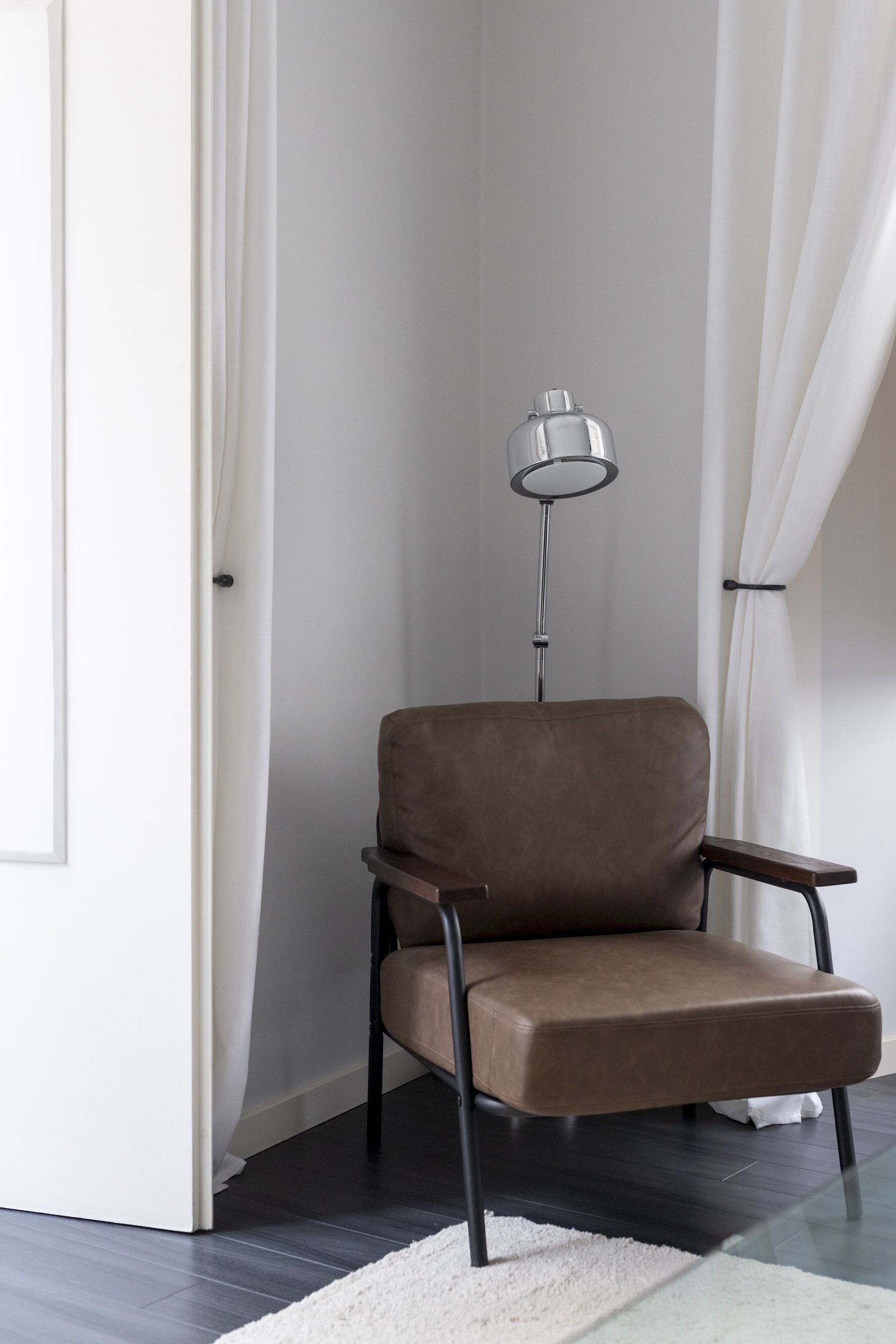 A modern room with a brown leather chair, a floor lamp, and a white rug.