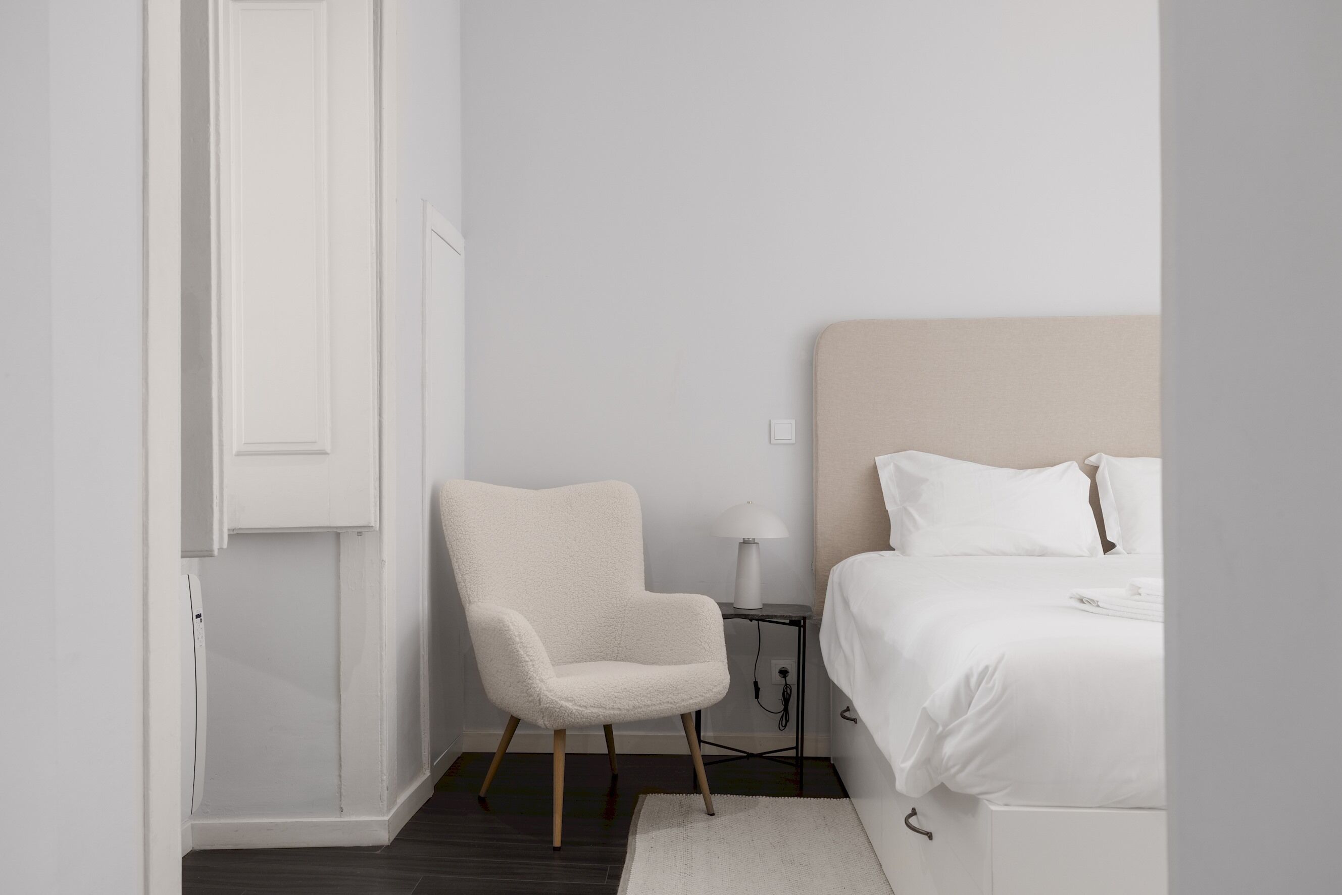 Een minimalistische slaapkamer met een bed, een stoel en een nachtkastje.