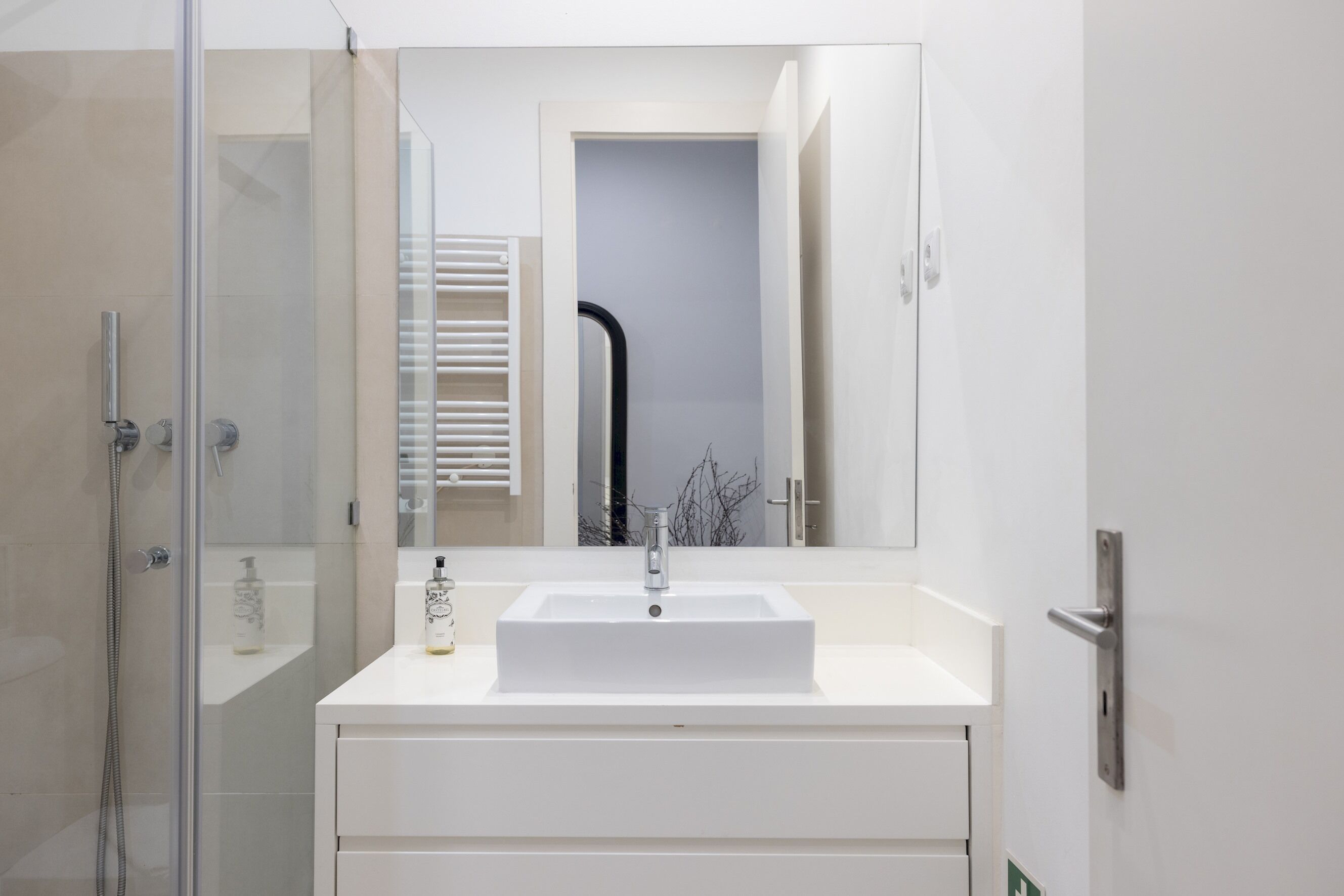 A modern bathroom with a white sink, a glass shower enclosure, and a large mirror.