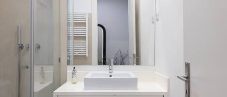 A modern bathroom with a white sink, a glass shower enclosure, and a large mirror.