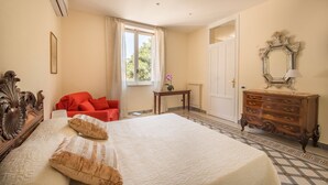 Een slaapkamer met een groot bed, een houten dressoir, een rode stoel en een raam met gordijnen.