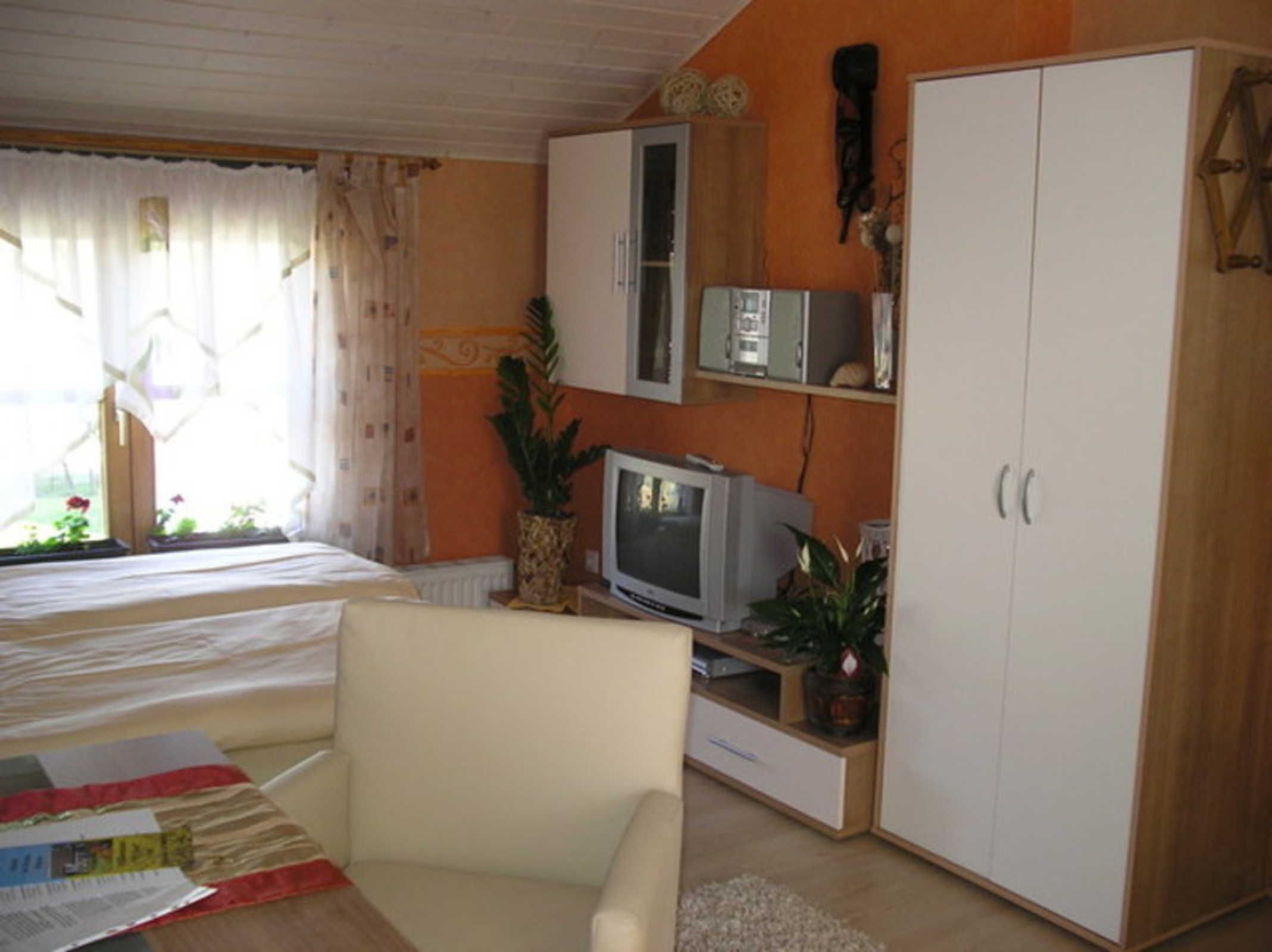 A bedroom with a bed, a TV, a wardrobe, and a window with curtains.
