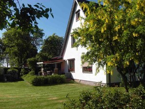 A white house with a sloped roof, surrounded by a well-maintained lawn and various trees. - Fewo 3 - holiday home To Hus WE143 (Thesenvitz)