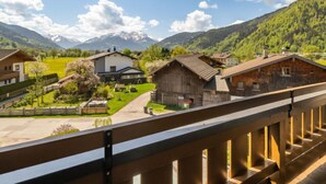 Un village de montagne aux maisons traditionnelles en bois, sous un ciel dégagé, avec en toile de fond des montagnes enneigées.