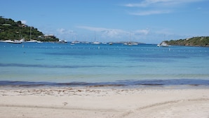 Una playa con agua azul cristalina, barcos y una orilla arenosa.