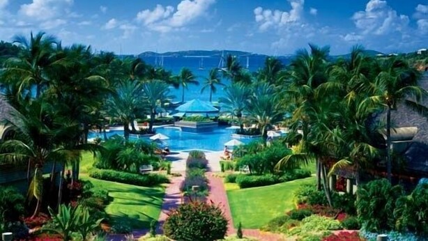 Un resort con piscina central, rodeado de palmeras y un cielo despejado.