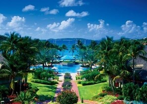 Een resort met een centraal gelegen zwembad, omringd door palmbomen en een heldere lucht.
