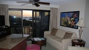 Habitación de hotel con balcón, sofá, mesa de centro y televisor.