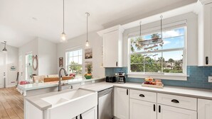 Cozinha moderna com armários brancos, uma janela grande com vista para o verde e uma planta pendente.