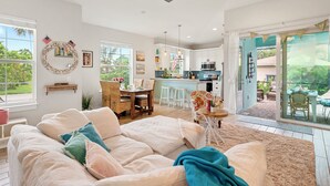 Uma sala de estar espaçosa com um amplo sofá bege, um espaço de jantar com mesa e cadeiras de madeira, uma cozinha com eletrodomésticos modernos e grandes janelas com vista para o exterior.