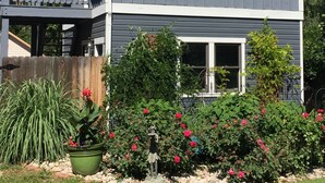 Ein zweigeschossiges Haus mit Balkon, Veranda und einem Garten mit Blumen und Sträuchern.