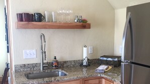 Eine Küche mit Granitarbeitsplatten, Holzschränken, einem Edelstahlkühlschrank und einem Holzregal über der Spüle.