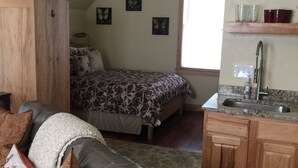Ein gemütliches Zimmer mit Bett, einer Couch, einer Küchenzeile und einem Fenster.