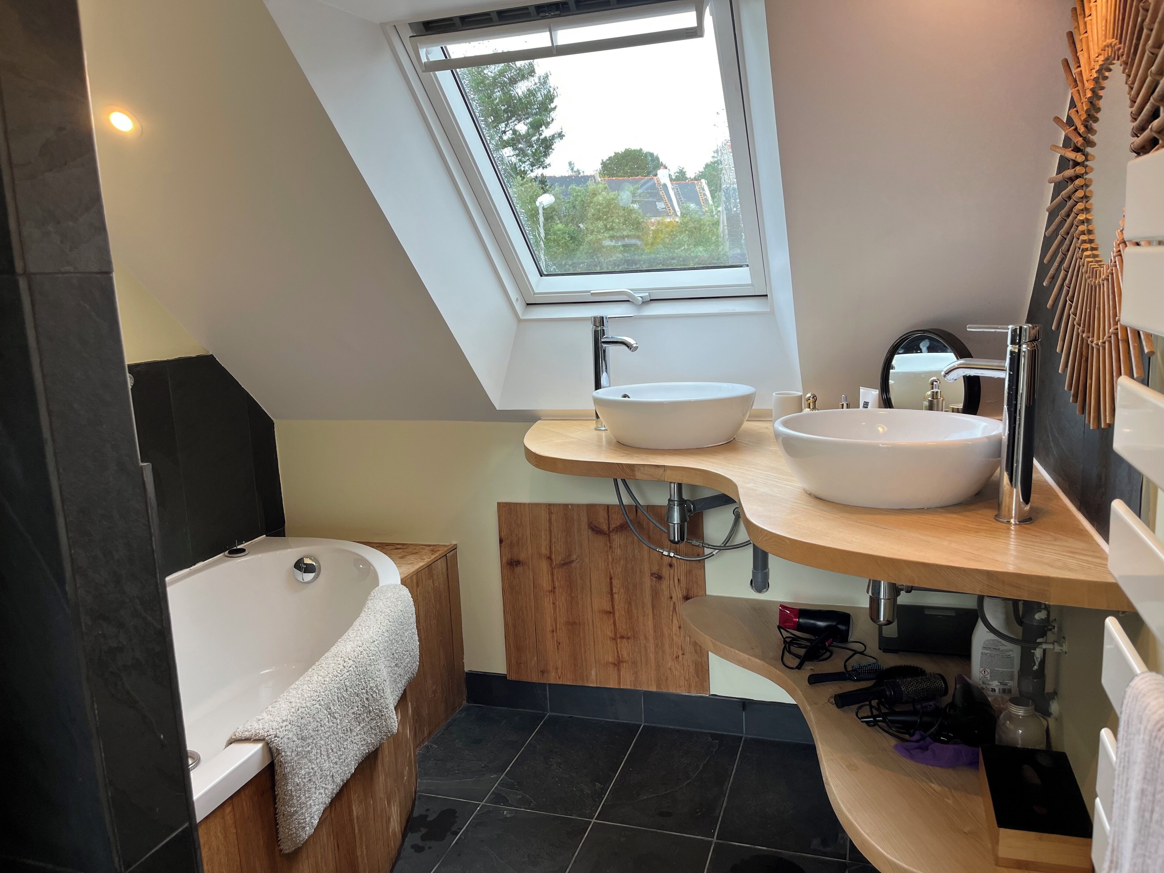 A modern bathroom with a skylight, two sinks, a bathtub, and a wooden vanity.