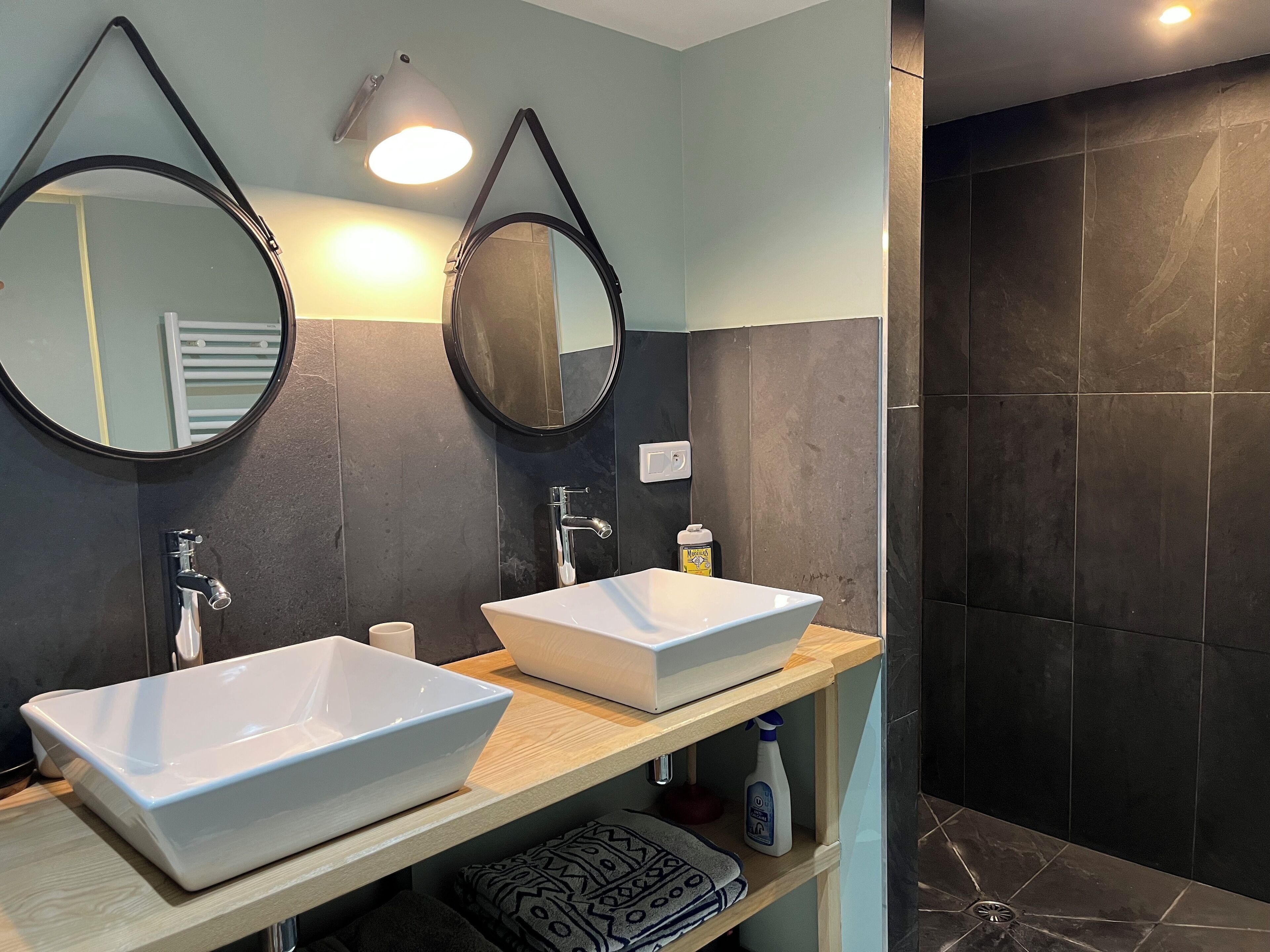 A modern bathroom with two white sinks, a mirror, and a shower area.