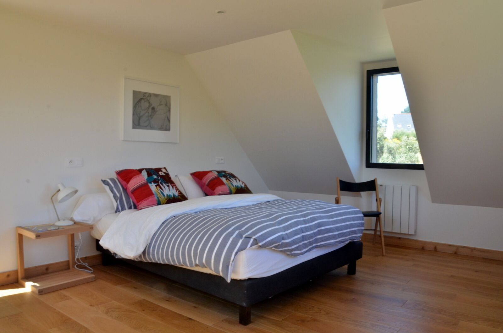 A bedroom with a bed, a desk, a chair, a window, and a radiator.