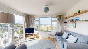 A modern living room with a large window, a flat-screen TV, a sofa, and a small table. - E28 HI-Up, Riviere Towans (Hayle)