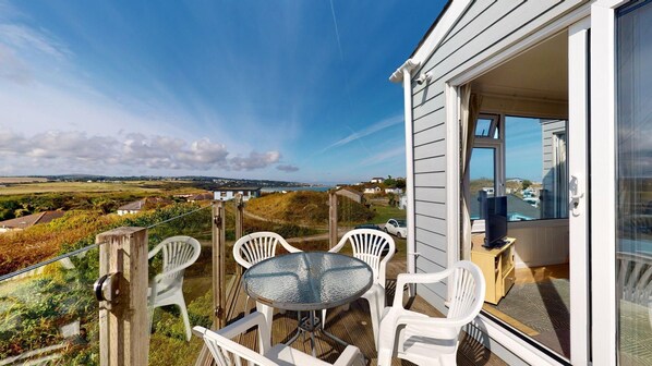 A balcony with a glass door, white plastic chairs, and a round table. - E28 HI-Up, Riviere Towans (Hayle)