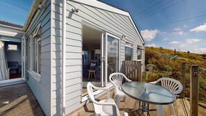 A small, single-story house with a deck, a glass door leading to a living area, and a view of the surrounding landscape. - E28 HI-Up, Riviere Towans (Hayle)