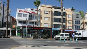 Vista de la calle con una pizzería llamada DolceVita, una farmacia y un edificio con balcones.