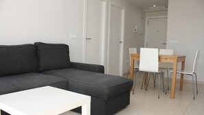 Una sala moderna con un sofá seccional gris, una mesa de centro blanca y un comedor con mesa de madera y sillas blancas.