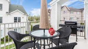 Ein Balkon mit rundem Tisch, Korbstühlen, einem Grill und einer Zierkanne.