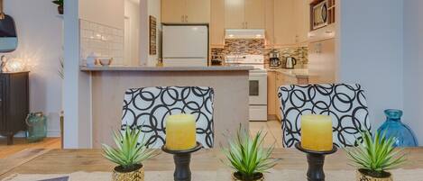 A modern kitchen with wooden cabinets, a central island, and a dining area with patterned chairs and candles.