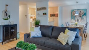 Ein modernes Wohnzimmer mit grauem Sofa, einem dunklen Holzschrank und einem Essbereich mit gemusterten Stühlen.
