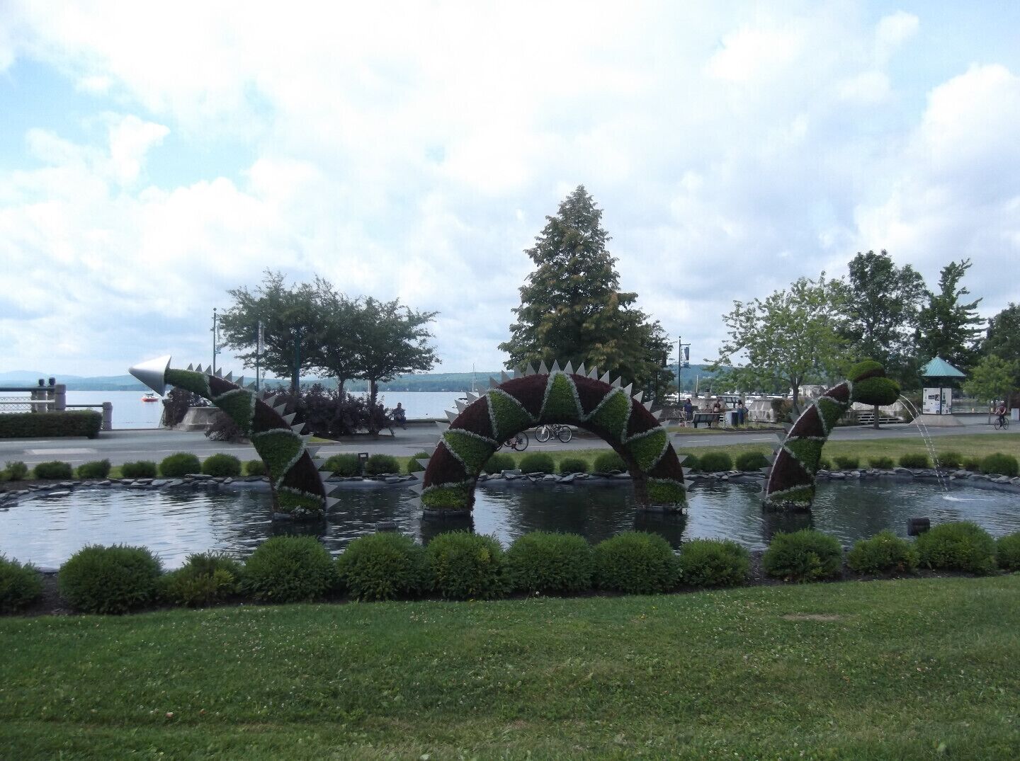 A park with a pond, a large tree, and a bridge-like structure.