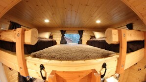 A circular wooden room with a bed centered, wooden walls, and a window at the back.