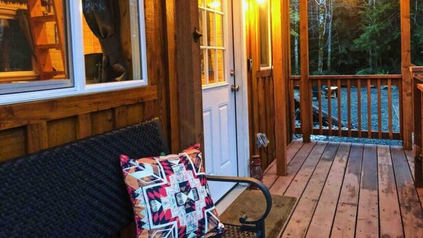 A wooden porch with a bench and a door, surrounded by a wooden railing and string lights.
