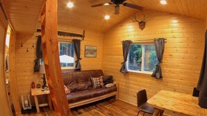 A cozy cabin interior with a wooden floor, a sofa, a dining table, and a ceiling fan.
