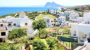 A coastal residential area with white buildings, a golf course, and a mountain in the background.