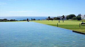 A pool with clear water, a grassy area, and a view of the sea.