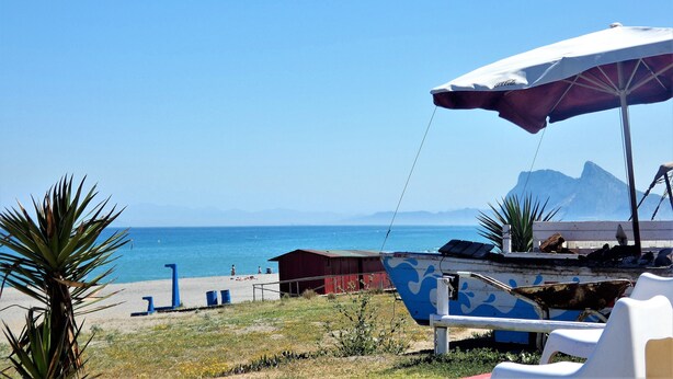 A beach scene with a clear sky, a red building, and a blue boat.