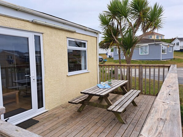 A wooden deck with a picnic table and chairs, a sliding glass door, and a small window.