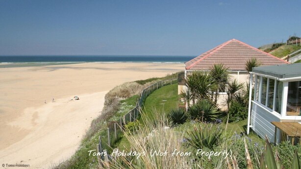 A beach house with a view of the ocean, a fenced garden, and a wooden deck.