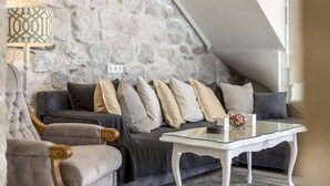 En hyggelig stue med en stenvæg, en mørkegrå sofa med mange puder, et hvidt sofabord og en lampe med et geometrisk mønster.