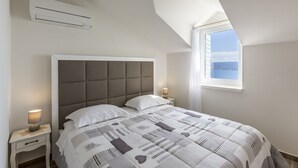Et soveværelse med en stor seng, et vindue med udsigt, et natbord med lampe og en aircondition.