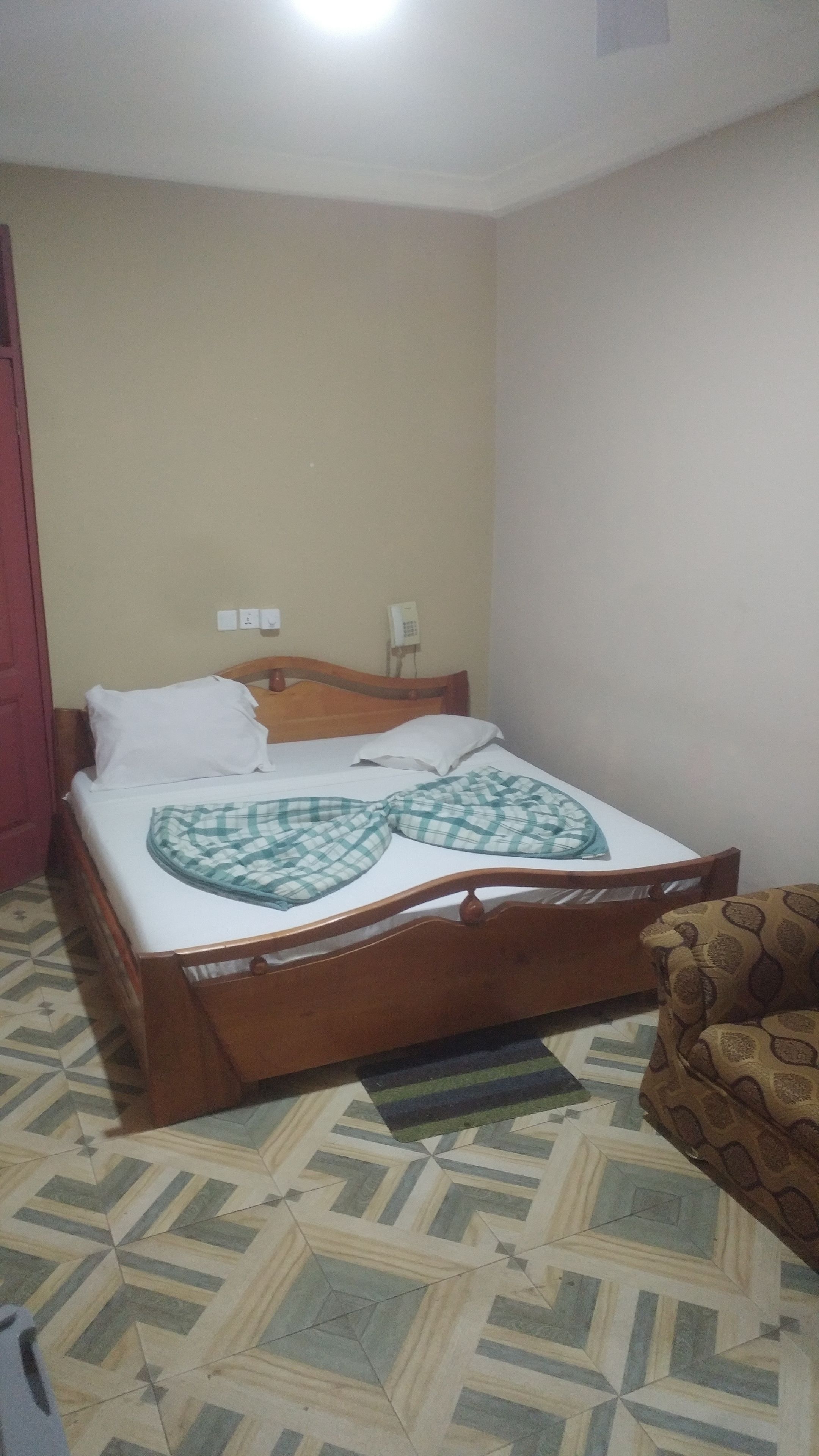 Um quarto com uma cama, um tapete estampado, uma cabeceira de madeira e uma cadeira estampada.