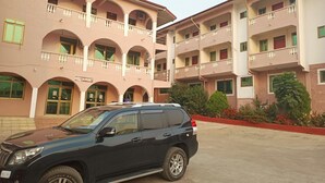 Un edificio de varios pisos con un restaurante en la planta baja, con balcones y un estacionamiento donde se aprecia un SUV negro.