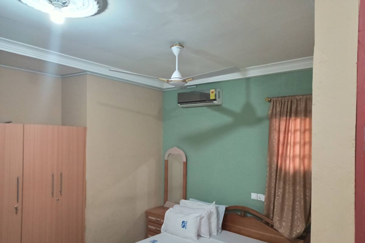 Ein Schlafzimmer mit Bett, Kleiderschrank, Deckenventilator und einem Fenster mit Vorhängen.