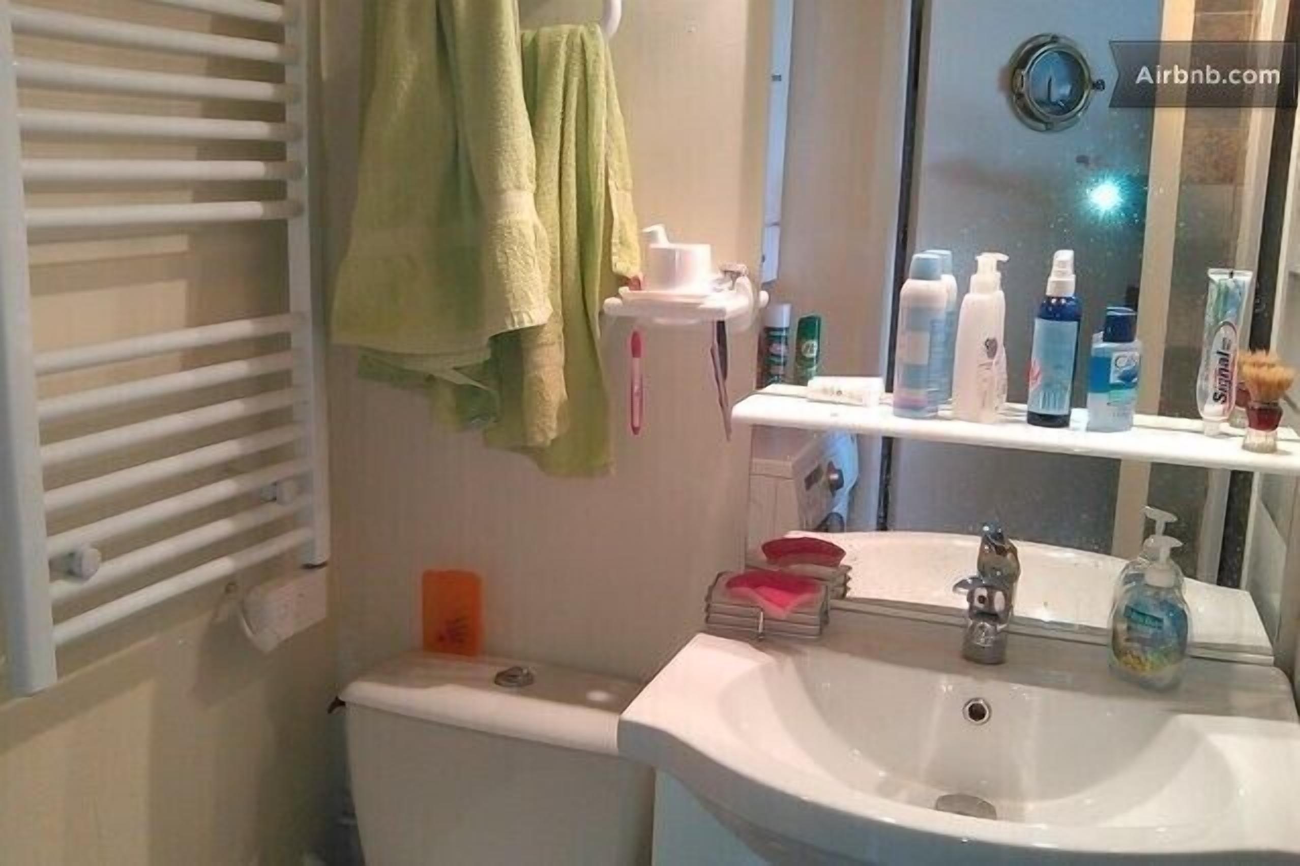 Une salle de bain équipée de toilettes, d’un lavabo et d’un porte-serviettes. On trouve des articles de toilette sur le comptoir du lavabo.